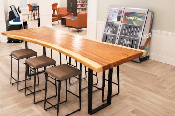 Long natural wood countertop with stools in front of laptop dispenser